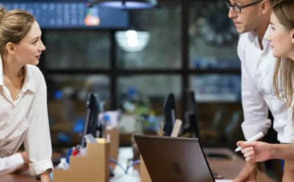 Three business colleagues discussing IT change management decisions around a computer table in a modern office.