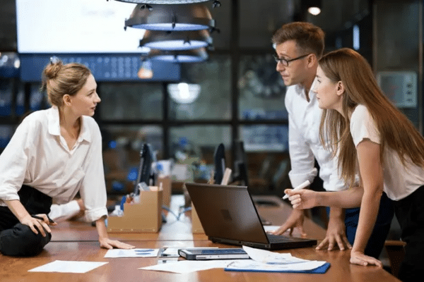 Three business colleagues discussing IT change management decisions around a computer table in a modern office.