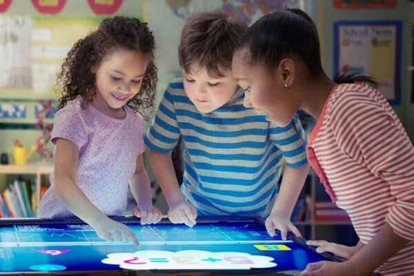 Three elementary students collaborating on an interactive touchscreen display in a Chicago classroom, demonstrating technology-driven learning and teamwork.