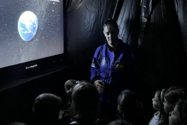 Teacher guiding students in a Chicago school makerspace lunar exploration activity using an interactive display panel to view Earth from space during a STEAM learning project.