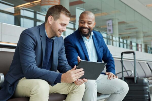 Business professionals using a tablet while traveling through an airport, highlighting cybersecurity considerations related to remote work, public Wi-Fi, and major public events