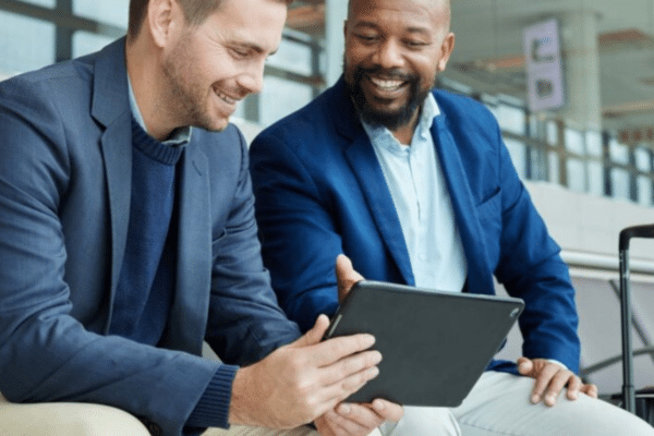 Business professionals using a tablet while traveling through an airport, highlighting cybersecurity considerations related to remote work, public Wi-Fi, and major public events
